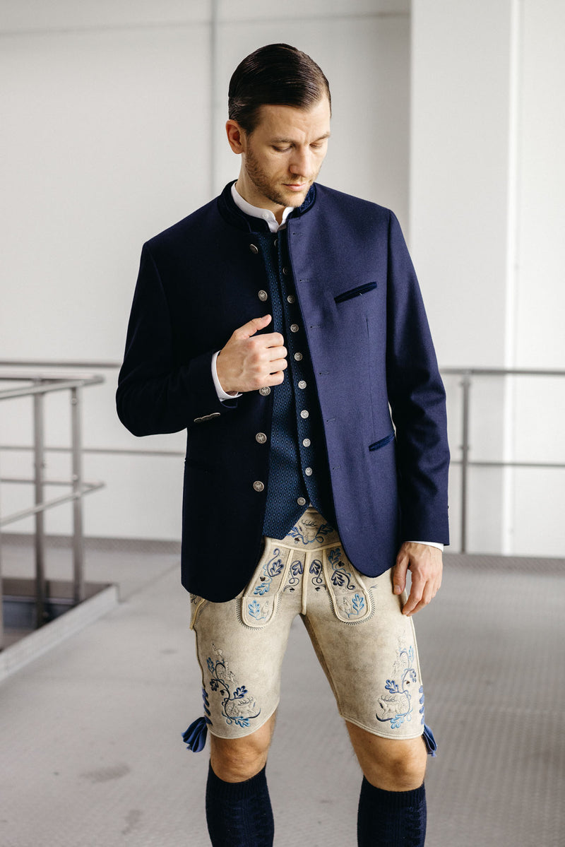 Trachtenoutfit mit dunkelblauem Janker, dunkelblauer gemusterter Trachtenweste mit Münzknöpfen und heller Lederhose aus sämisch gegerbtem Leder mit blauer Stickerei.