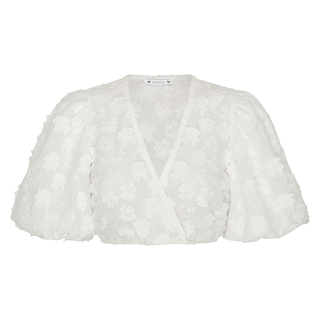 Weiße Dirndlbluse aus transparenter Spitze mit floralem Muster und Wickeloptik. Das Modell verfügt über einen tiefen V-Ausschnitt, kurze Puffärmel mit elastischen Abschlüssen und einen leicht verkürzten Schnitt. Die feine Blütenstickerei verleiht der Bluse eine elegante und romantische Optik.