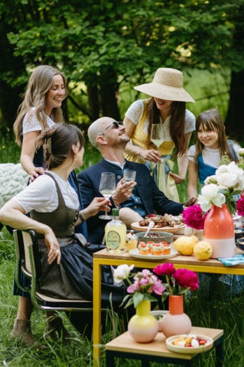 Hochzeitsgäste in eleganter Tracht bei einer sommerlichen Feier im Grünen; festliche Dirndl- und Janker-Looks von Amsel Fashion.