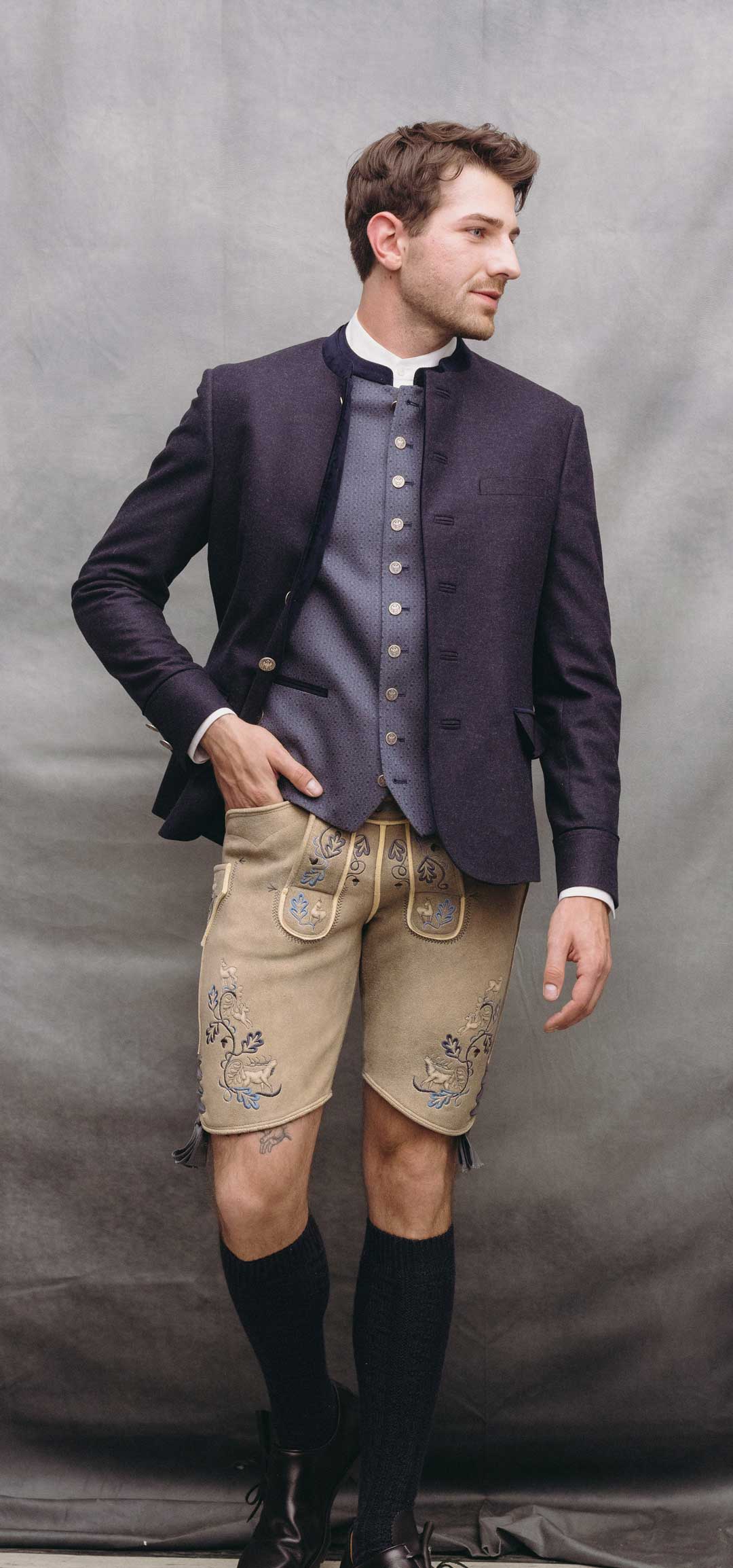 Trachtenoutfit mit dunkelblauem Janker, hellblauer gemusterter Trachtenweste und heller Lederhose aus sämisch gegerbtem Leder mit blauer Stickerei.