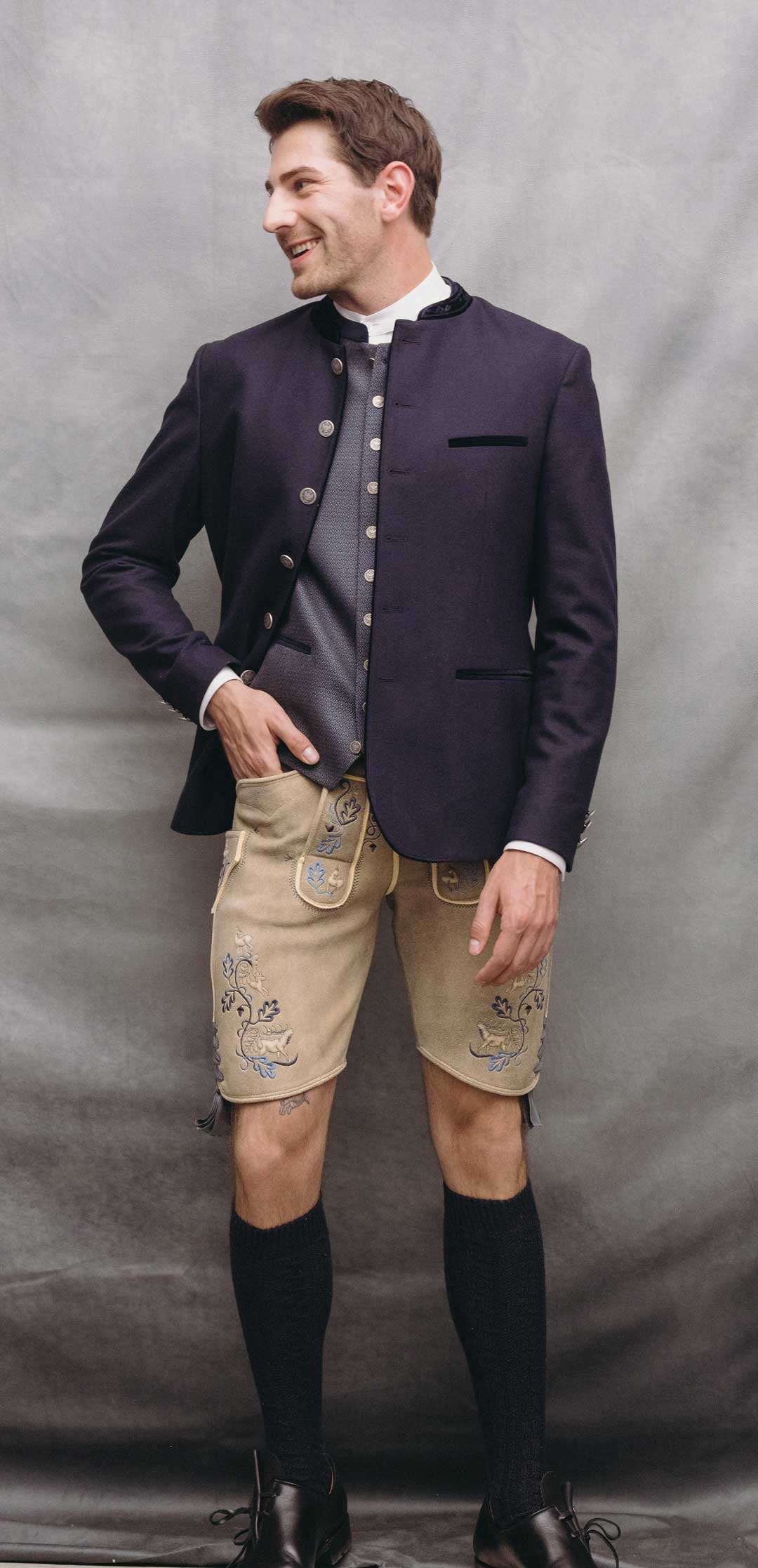 Trachtenoutfit mit dunkelblauem Janker, hellblauer gemusterter Trachtenweste und heller Lederhose aus sämisch gegerbtem Leder mit blauer Stickerei.
