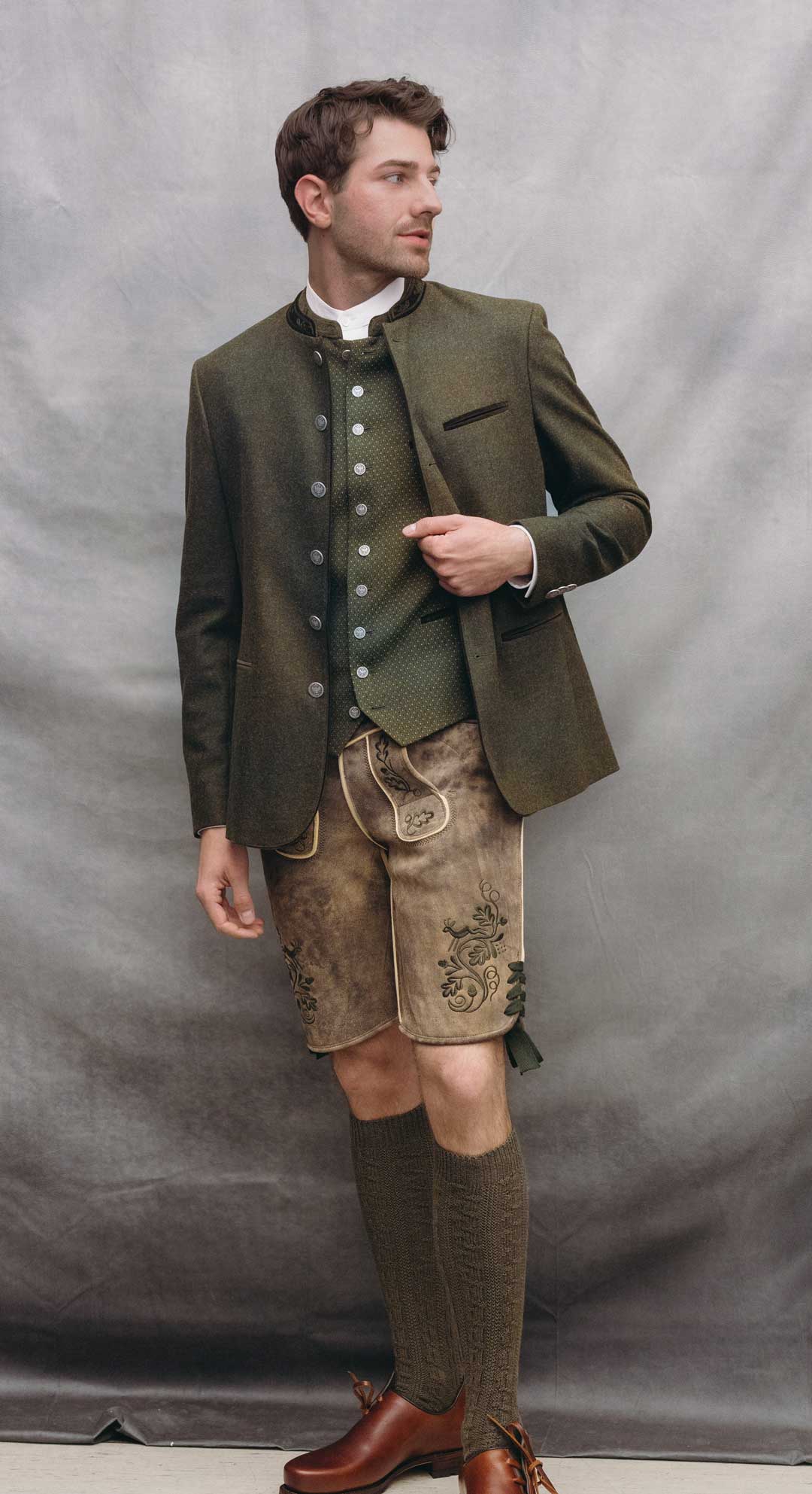 Trachtenoutfit mit olivgrünem Janker, gemusterter Trachtenweste in Olivgrün und Lederhose aus sämisch gegerbtem Ziegenleder in Braun mit grüner Stickerei.