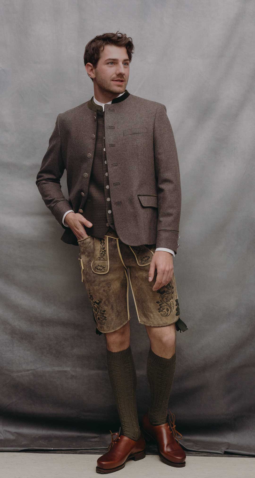 Trachtenoutfit mit schieferbraunem Janker, passender Trachtenweste mit Münzknöpfen und brauner Lederhose aus sämisch gegerbtem Ziegenleder mit dunkler Stickerei.