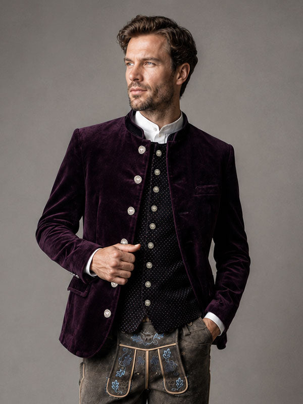Trachtenoutfit mit auberginefarbenem Samtjanker, dunkel gemusterter Trachtenweste mit Münzknöpfen und dunkler Hirschlederhose mit blauer Stickerei.