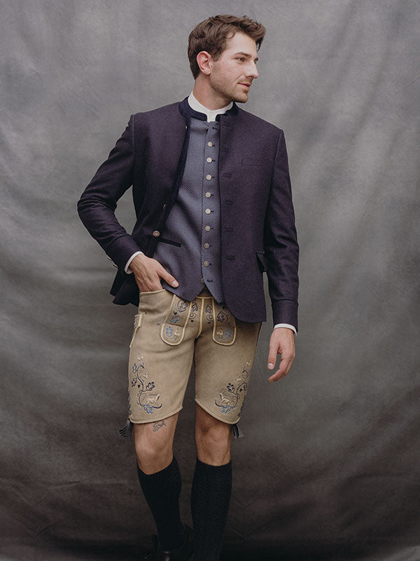 Herren-Trachtenoutfit mit dunkelblauem Janker, grauer Weste und heller Lederhose mit blauer Stickerei.