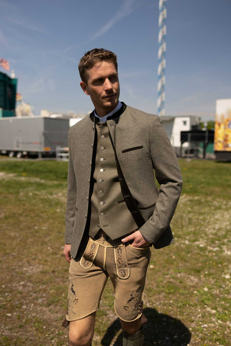 Mann in hellolivfarbener Weste mit silbernen Knöpfen und passendem Trachtenjanker mit dunklen Samtdetails, kombiniert mit heller bestickter Lederhose – eleganter Wiesn-Look auf dem Festplatz.